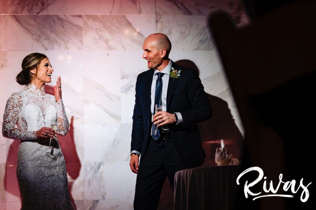 A candid, colorful picture of a groom looking at his bride in wonder as she laughs hysterically during a toast at their wedding reception at The Station at 28 Event Space in Kansas City.