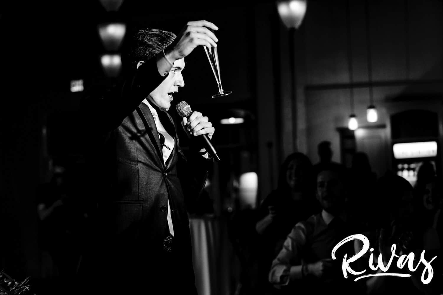 A candid black and white picture of the best man raising his toasting flute up into the air during a winter wedding reception at The Station at 28 Event Space. 