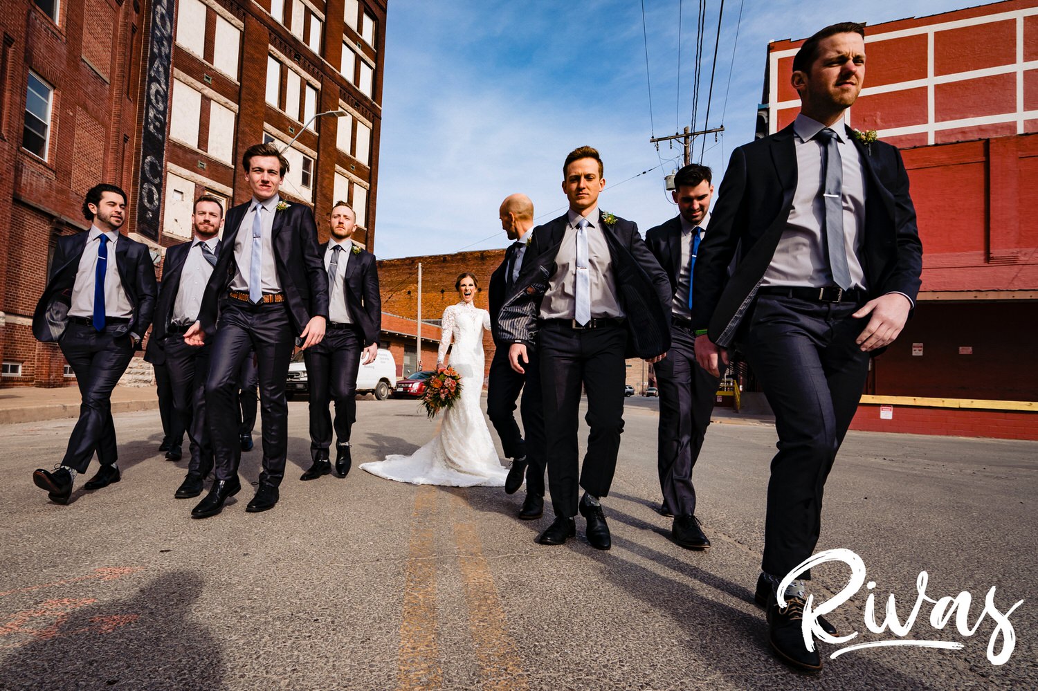 A wide, candid picture of a groom and his groomsmen walking by a bride and the camera on a sunny winter wedding day in Kansas City. 
