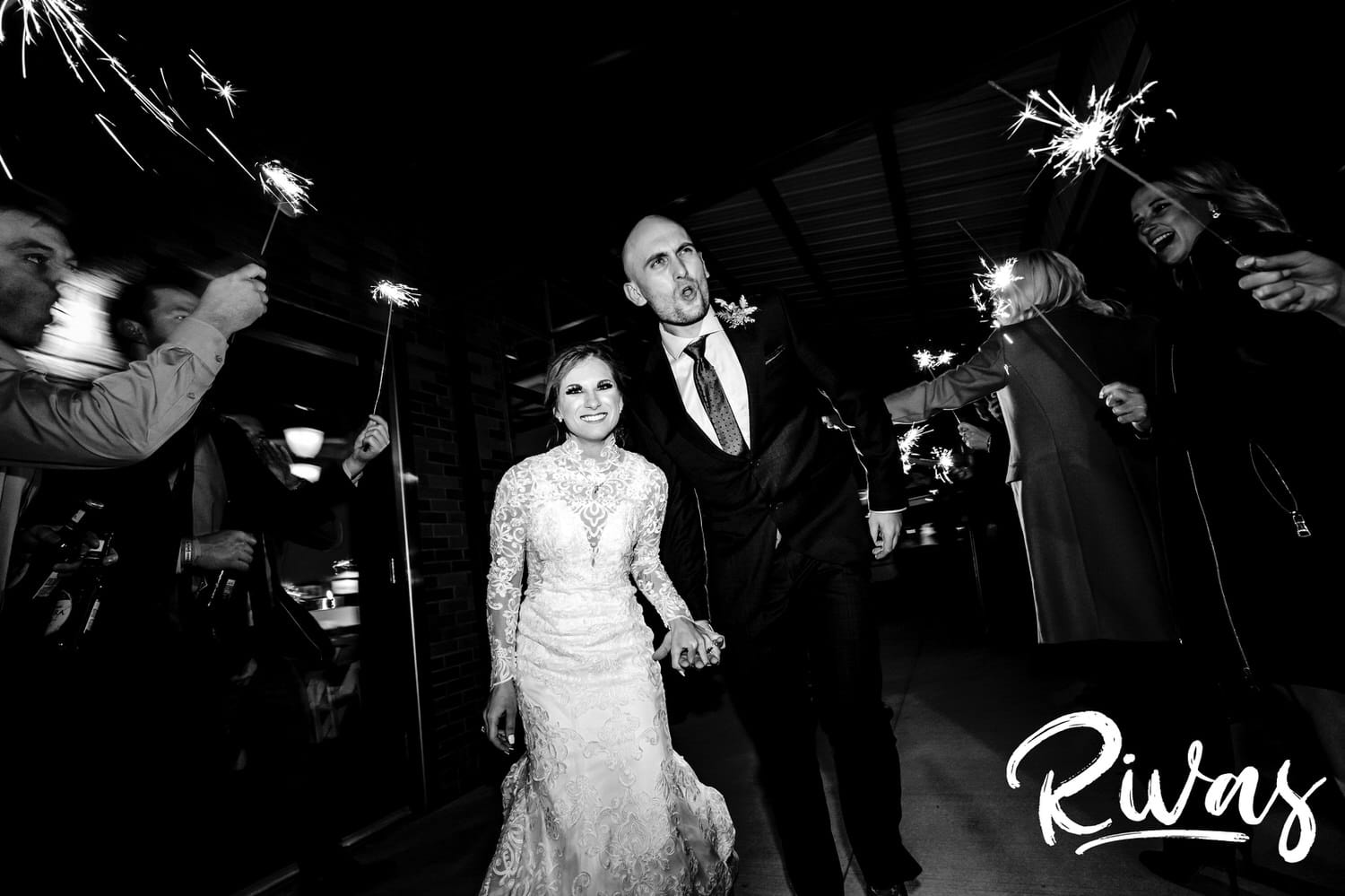 A candid black and white picture of a bride and groom exiting through an arch of sparklers at the end of their winter wedding day in Kansas City. 