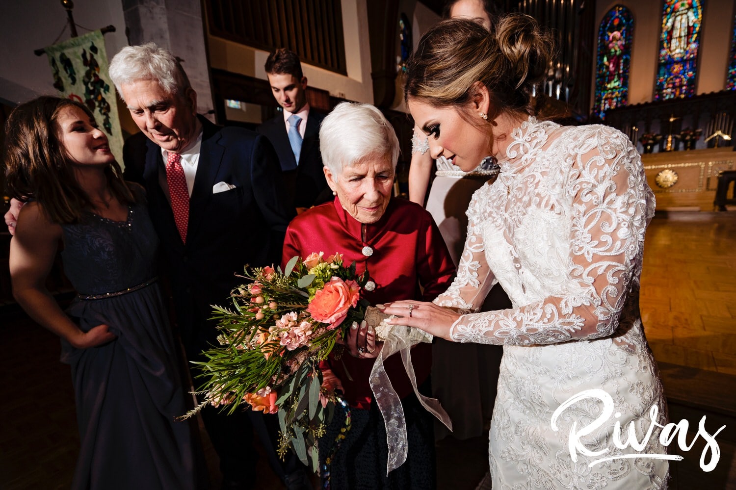 A candid, colorful picture of a bride showing her grandmother the lace wrapped around her bouquet's steps on her wedding day. 