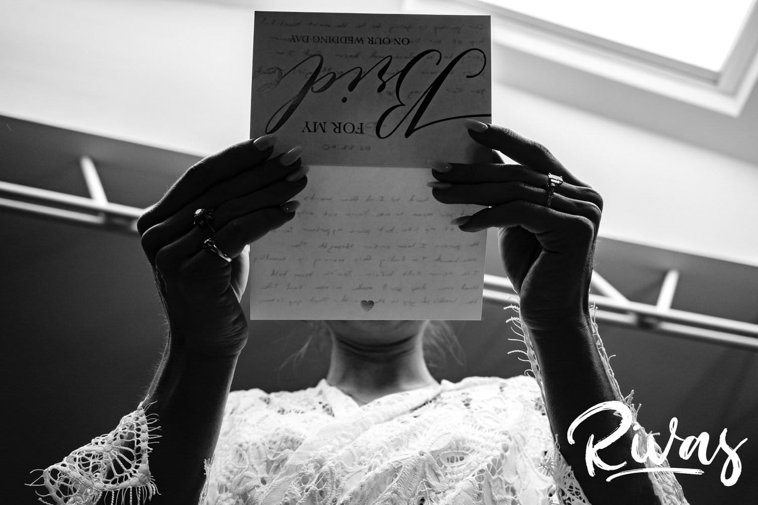 A candid black and white picture taken from the ground looking up of a woman reading a card that says "for my bride" on the front. 
