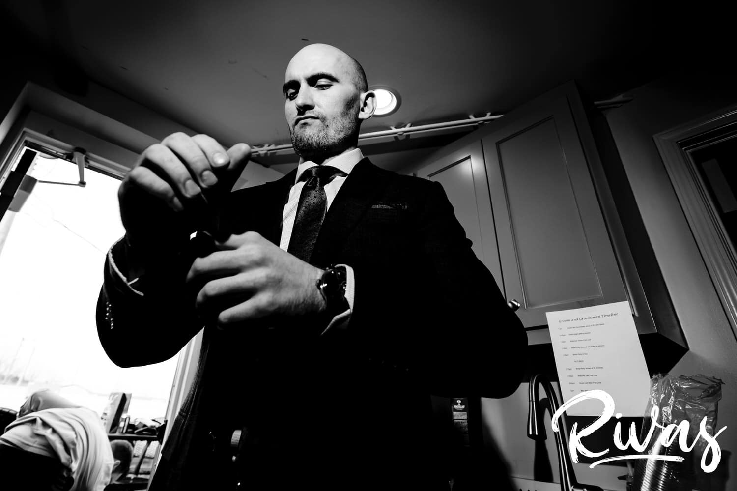 A candid black and white picture of a man in a suit working to pout his cufflinks on. 