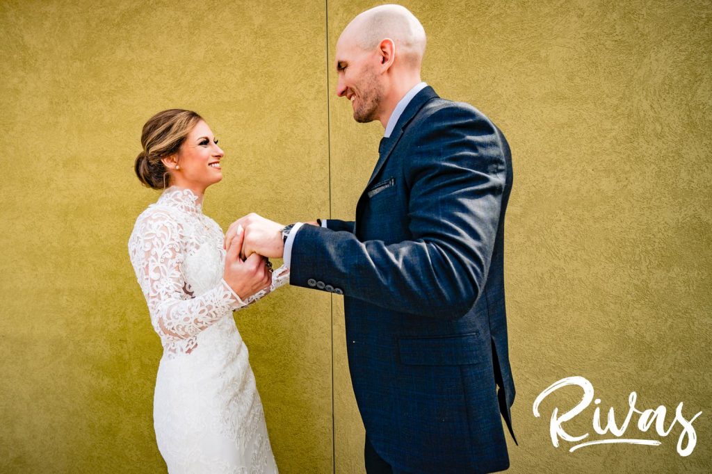 A candid, colorful picture of a bride and groom clasping hands as they share a first look together on the morning of their sunny winter wedding at The Station at 28 Event Space in Kansas City.