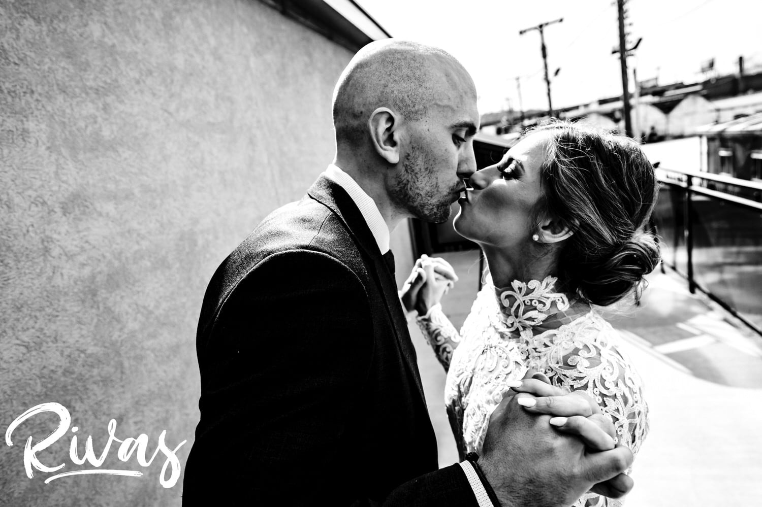 A candid, close-up black and white picture of a bride and groom grasping hands and sharing a kiss just after their first look at The Station at 28 Event Space on their winter wedding day. 