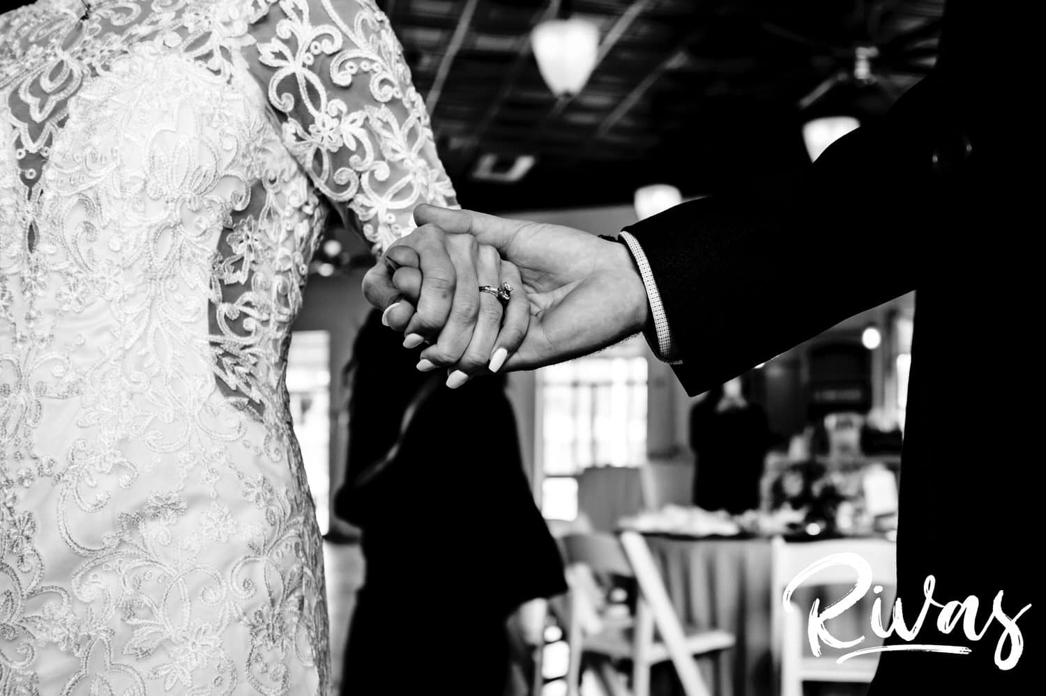 A close, black and white picture of a groom holding his bride's hand on the day of their wedding. 