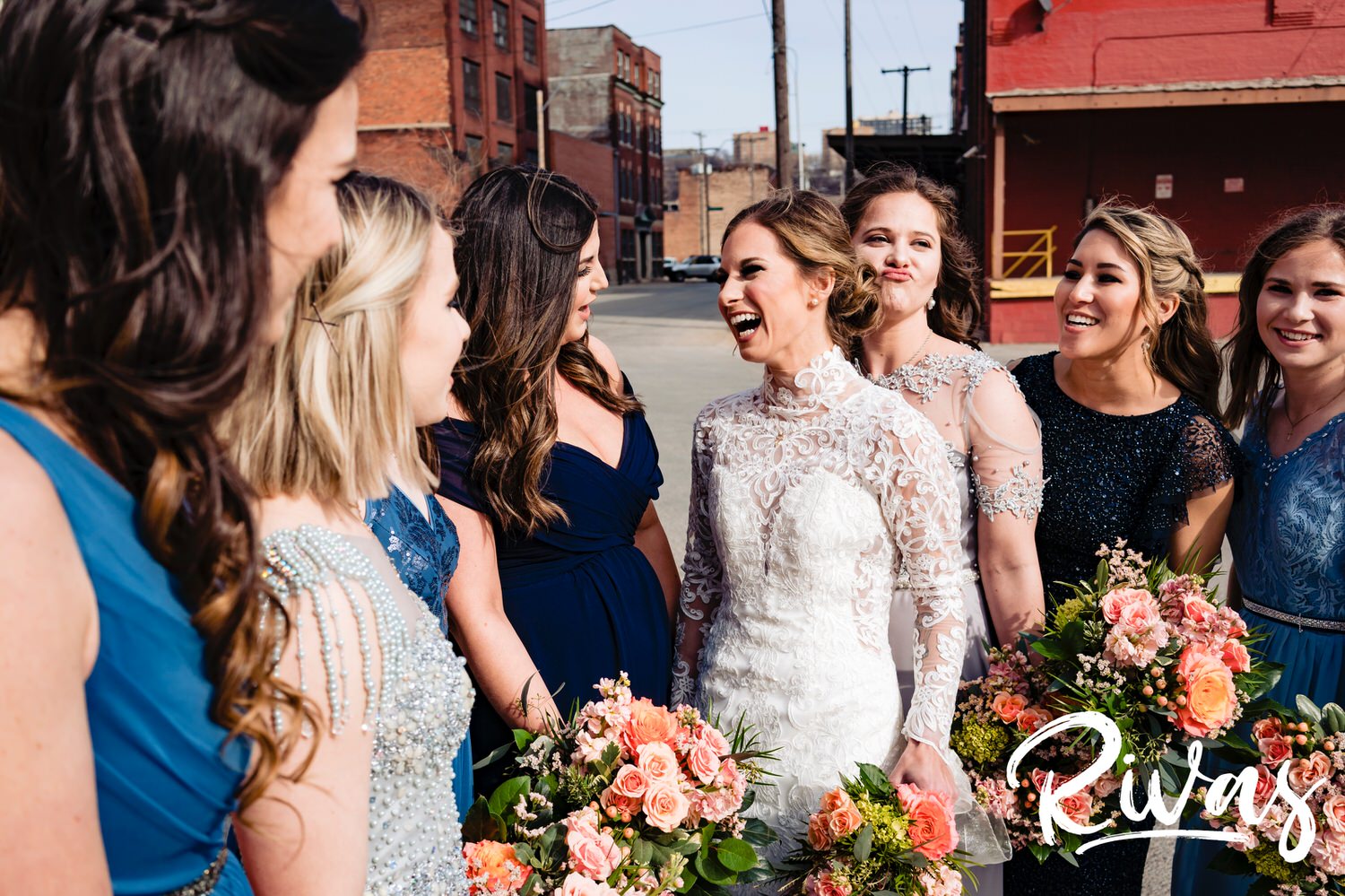 An up-close, candid picture of a bride laughing with her bridesmaids as they stand in the street of Kansas City's West Bottoms Neighborhood on a sunny winter wedding day in Kansas City. 