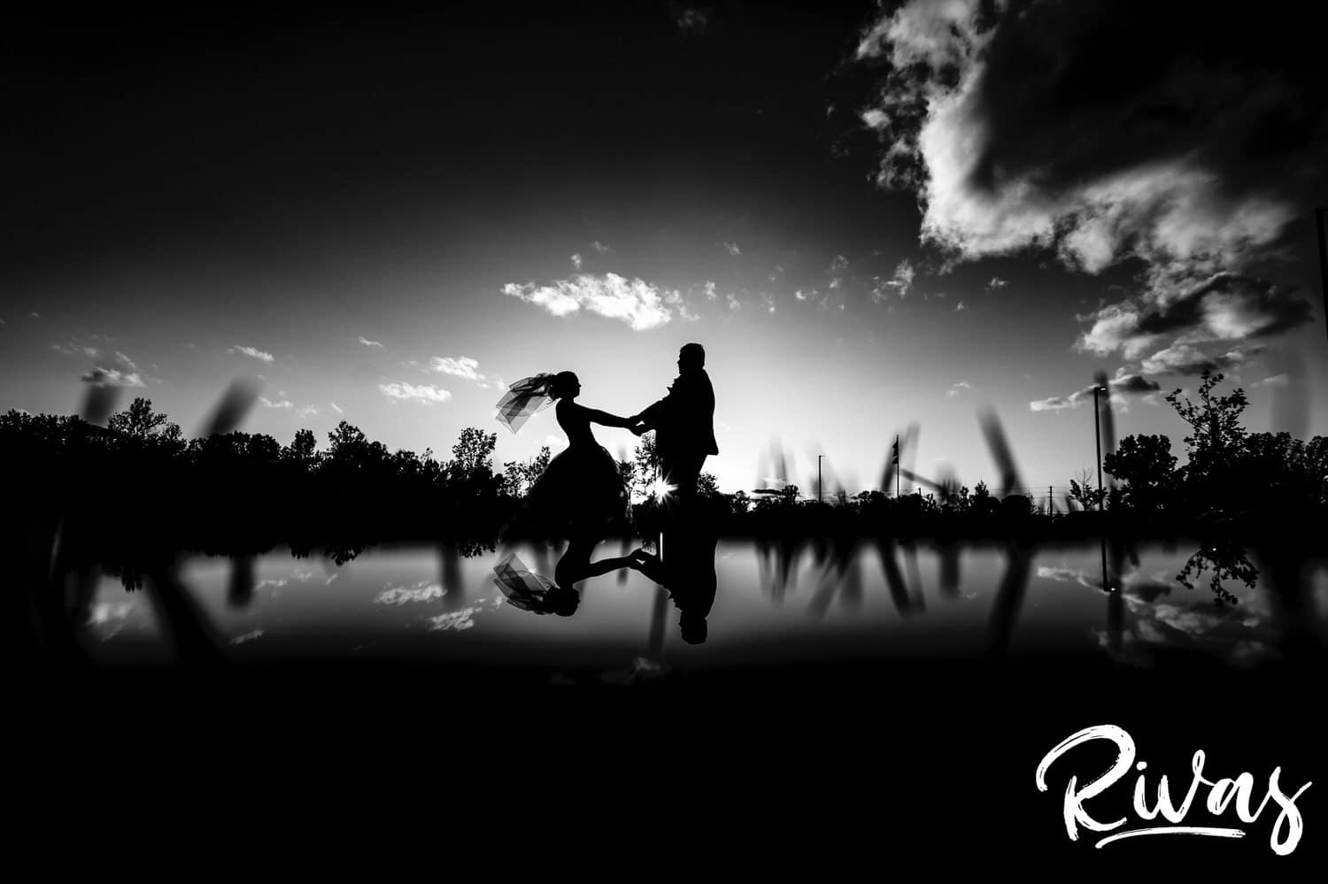A black and white silhouetted picture of a bride and a groom, tiny against the huge landscape, leaning in to share a kiss at sunset at Piazza Messina on their fall wedding day.