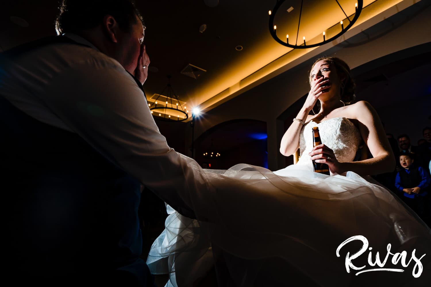 A candid picture taken from behind the groom of his bride, with her hand raised to her mouth in shock as he takes her garter off during their fall wedding reception at Piazza Messina. 
