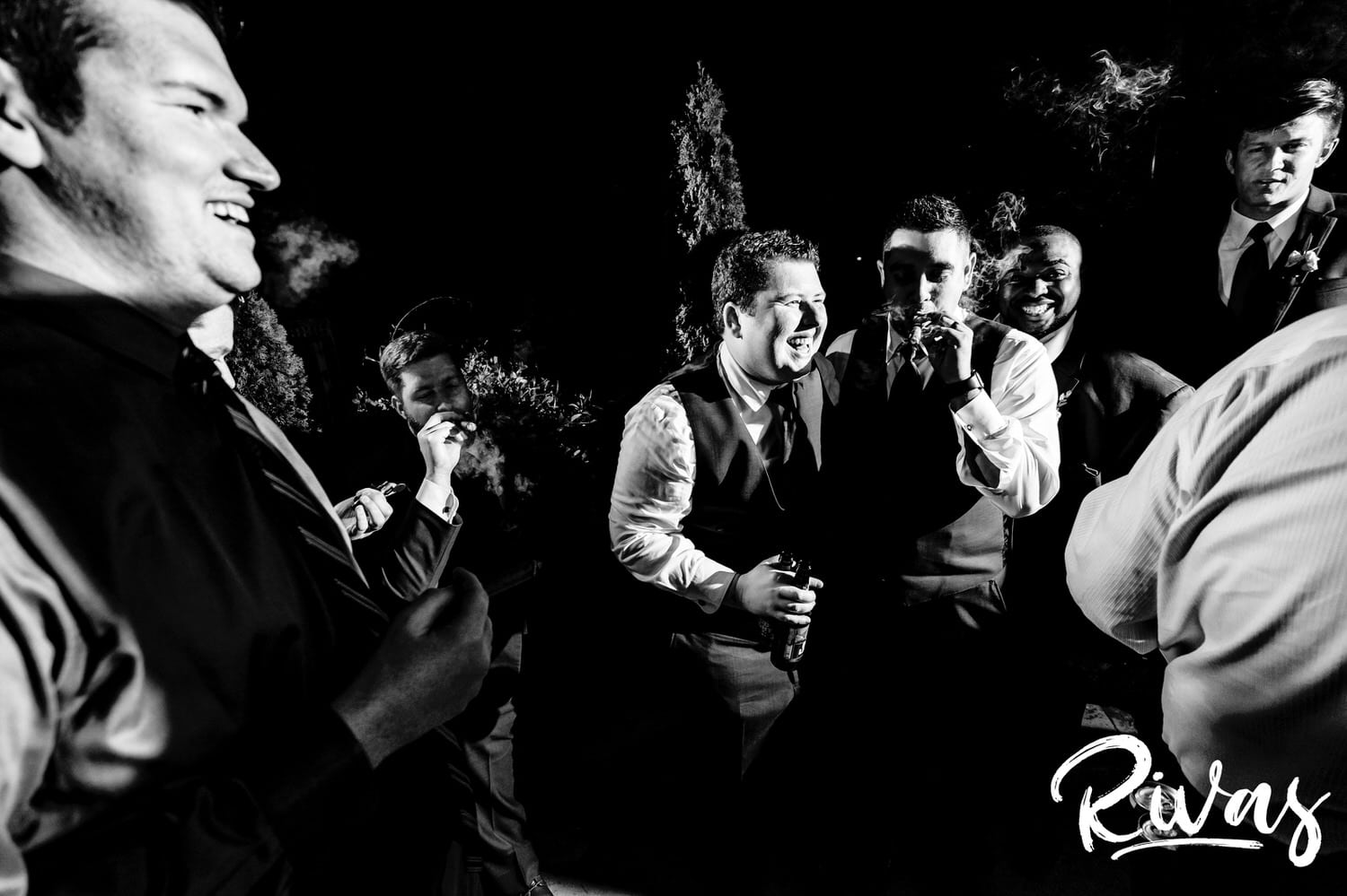 A candid black and white picture of a group of groomsmen smoking cigars on the patio of Piazza Messina during a fall wedding reception. 