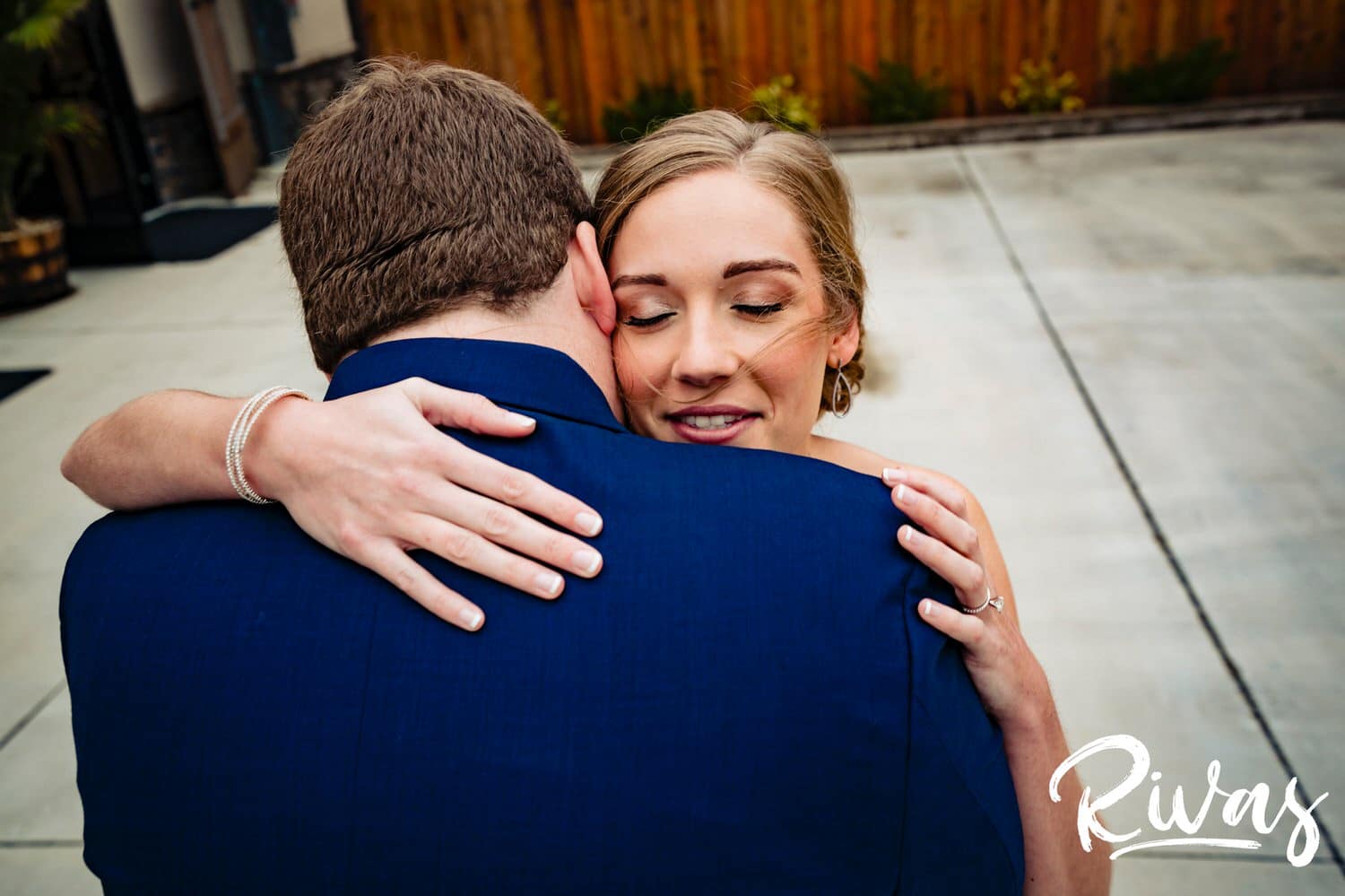 A colorful, candid picture taken over the shoulder of a groom in a blue tuxedo as his bride hugs him during their first look on their wedding day at Piazza Messina. 