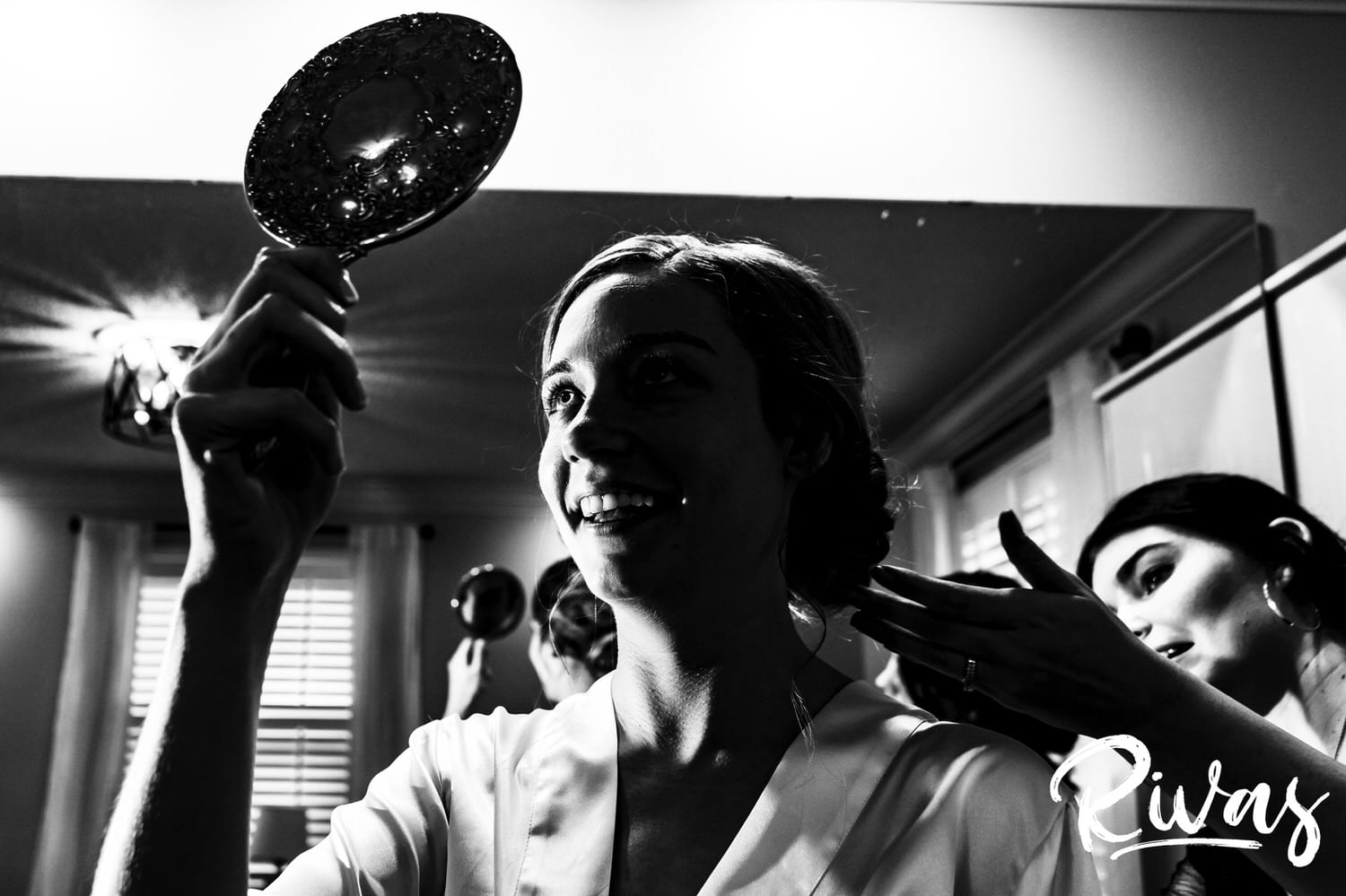 A candid black and white picture of a bride looking at the back of her hair in the mirror on her wedding morning at Piazza Messina in Cottleville, mO. 