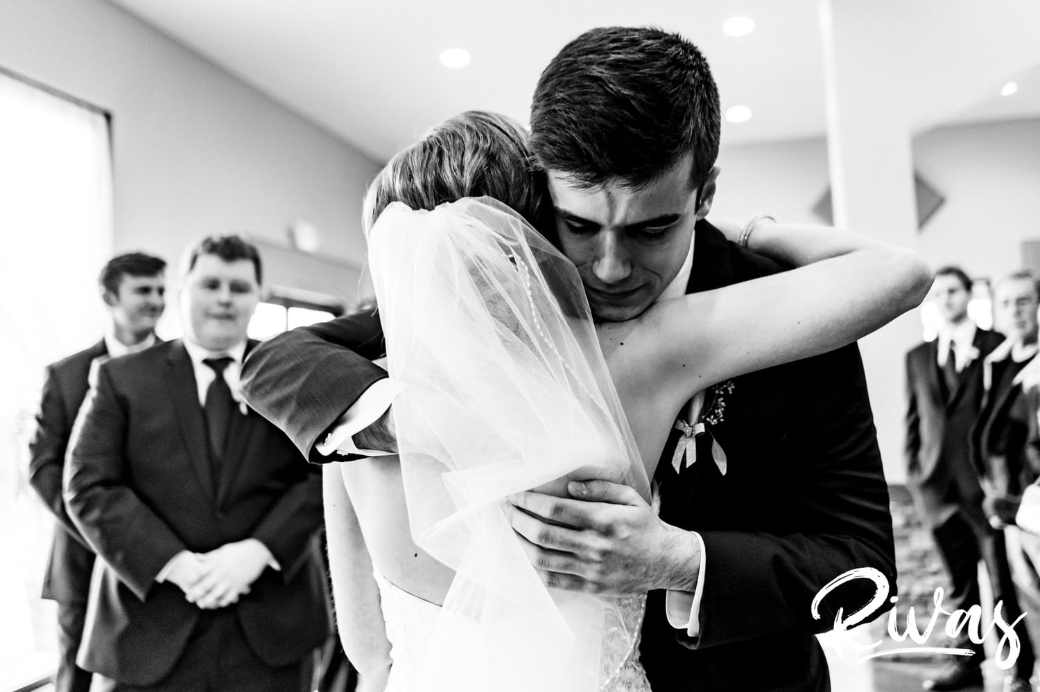 An emotional black and white picture of a bride's younger brother hugging her as he gives her away during her fall wedding ceremony at Piazza Messina in Cottleville, MO. 