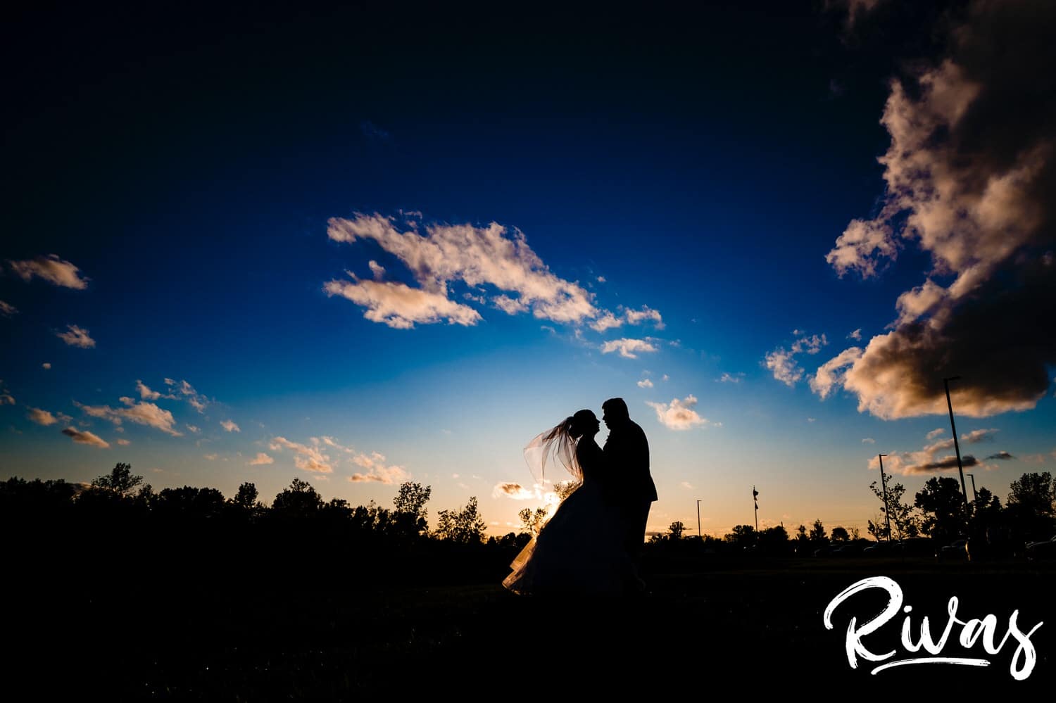 A silhouetted picture of a bride and a groom, tiny against the huge landscape, leaning in to share a kiss at sunset at Piazza Messina on their fall wedding day. 