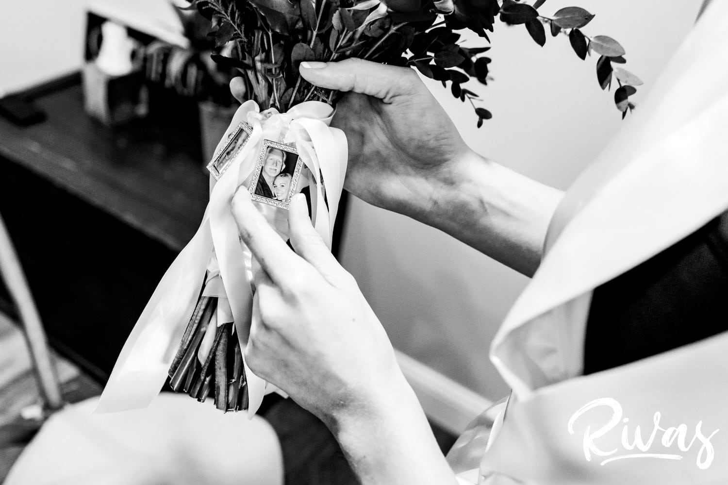 A black and white picture taken from the top looking down of a bride holding her bouquet, that displays a tiny framed photo of the bride and her late father on the morning of her fall wedding. 