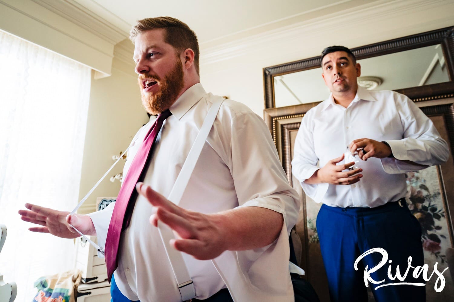 A candid picture of a groomsmen using his thumbs to pull his suspenders away from his body as he gets dressed on a fall wedding day in St. Louis. 