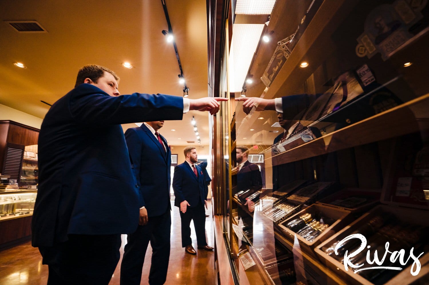 A candid picture of a groom and his groomsmen standing in front of a case of cigars on the day of his fall wedding at Piazza Messina. 