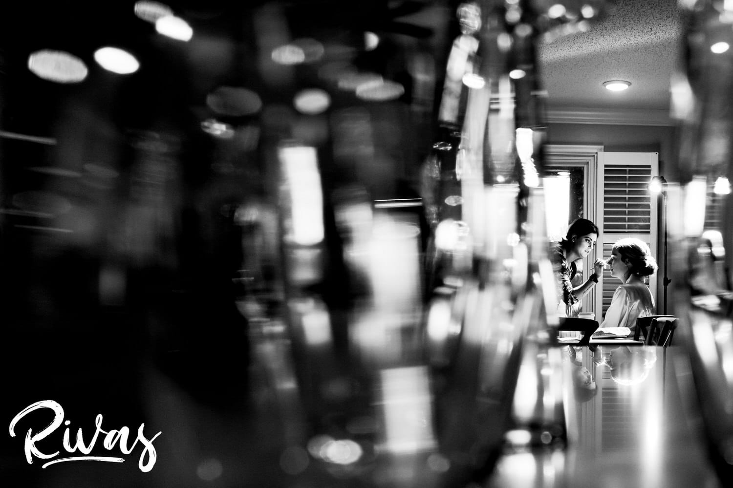 A black and white picture taken from a distance of a bride sitting at a table getting her wedding morning make-up done at Piazza Messina. 