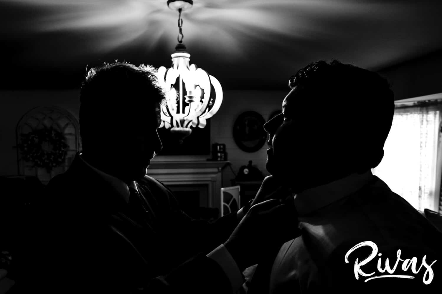 A dramatic black and white image of a groomsmen straightening the tie of a groom on his fall wedding morning. 