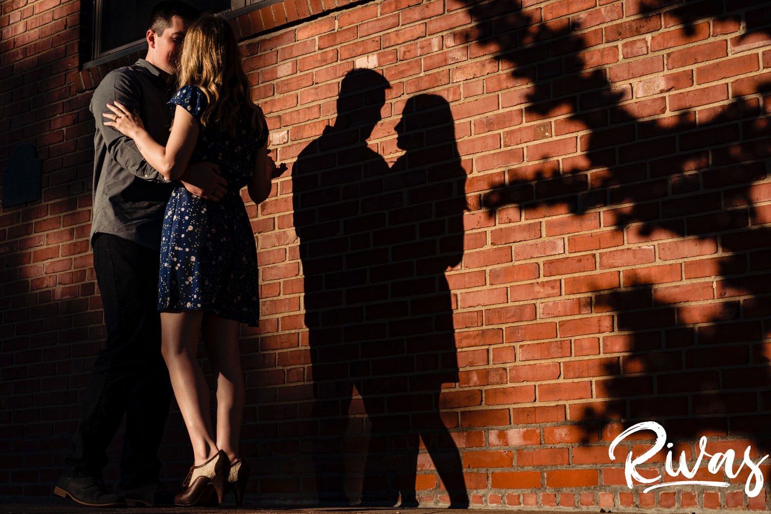 A bright, colorful image of an engaged couple dancing together, their shadow visible on the brick wall behind them during their City Market Summer engagement session in Kansas City. 