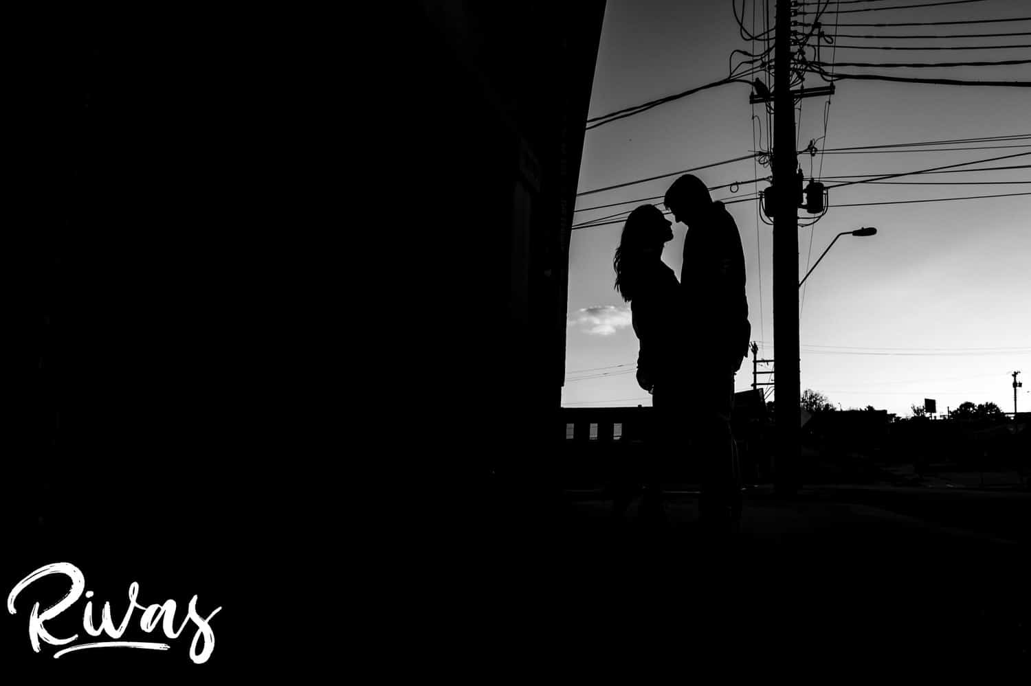 A bold black and white silhouette of an engaged couple sharing an embrace, looking at each other during their Kansas City summer engagement session. 