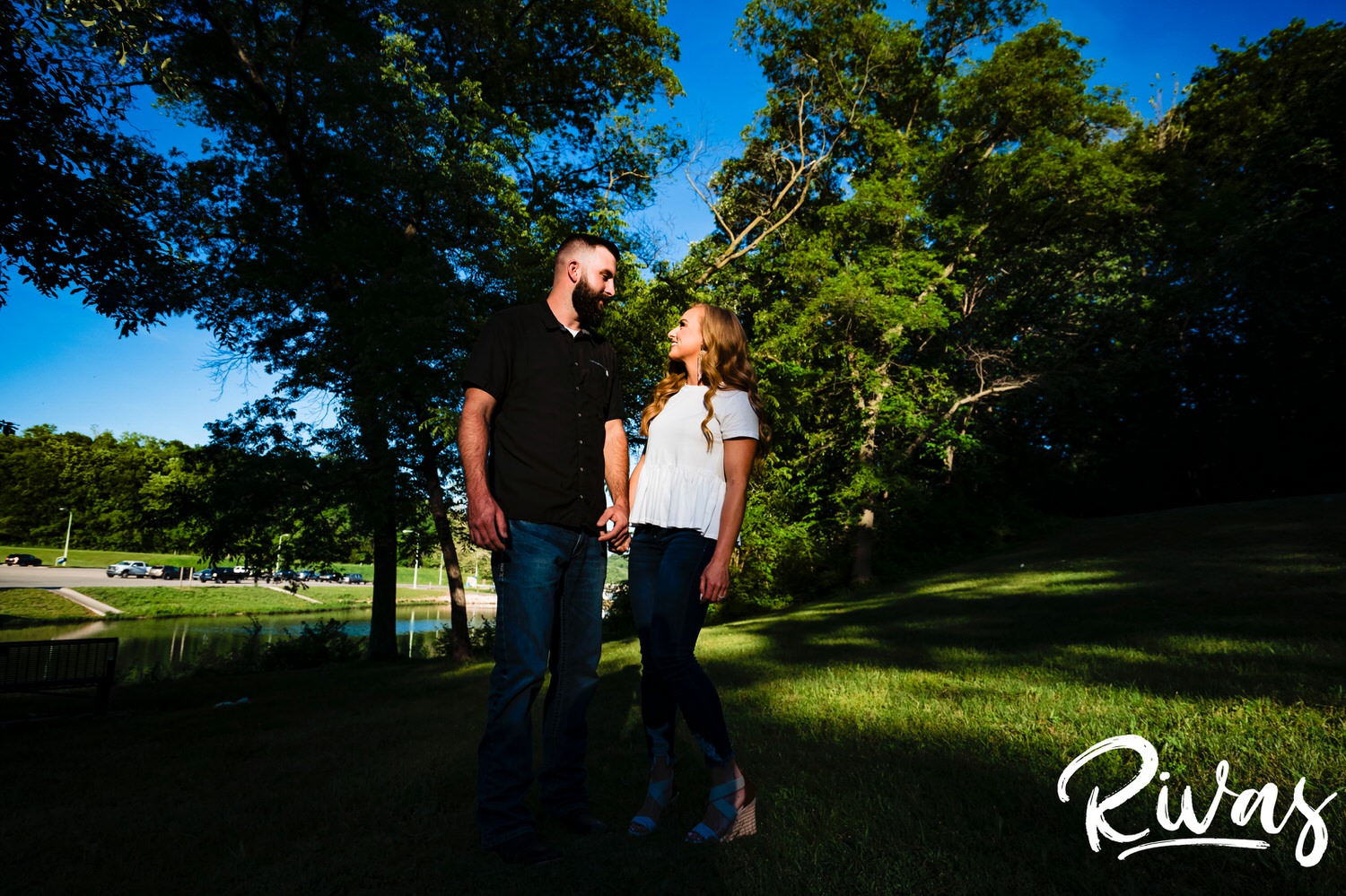 A vibrant portrait of an engaged couple holding hands, looking at each other surrounded by greenery during their summer engagement session in Kansas City. 