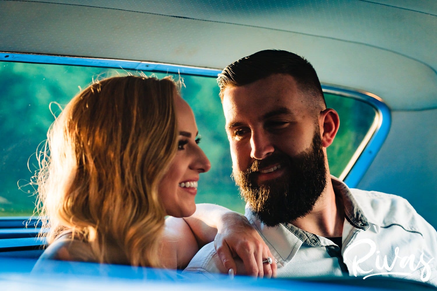 A candid, close-up picture taken through the window of a car of an engaged couple laughing together during their summer engagement session in Kansas City. 