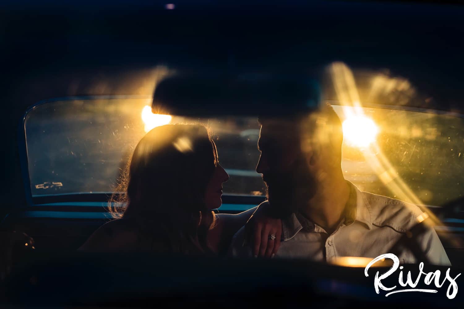 A dark and moody picture of an engaged couple leaning in to share a kiss as they sit in the back of a classic Impala during their summer engagement session in Kansas City. 