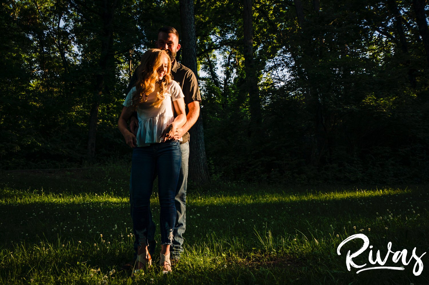 A colorful, dramatic portrait of a man hugging his fiance as he stands behind her as she laughs and looks off into the sunset during their summer engagement session. 