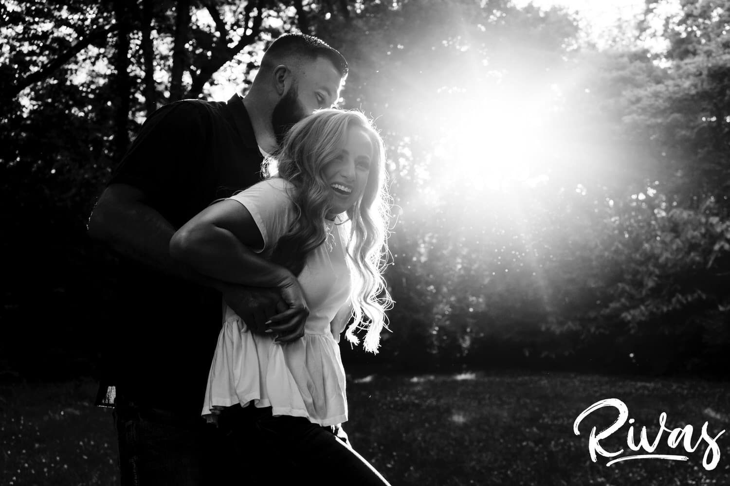 A candid black and white image of a man tickling his fiance as she laughs hysterically during their summer engagement session in Kansas City. 