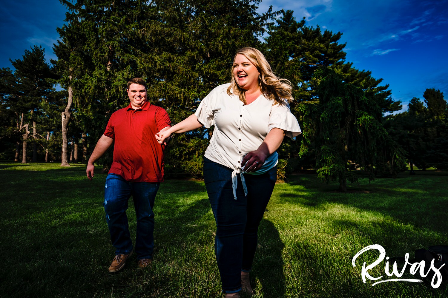 A colorful, candid picture of a woman running towards the camera, holding her fiance's hand as they both laugh during their engagement photography session in Kansas City. 