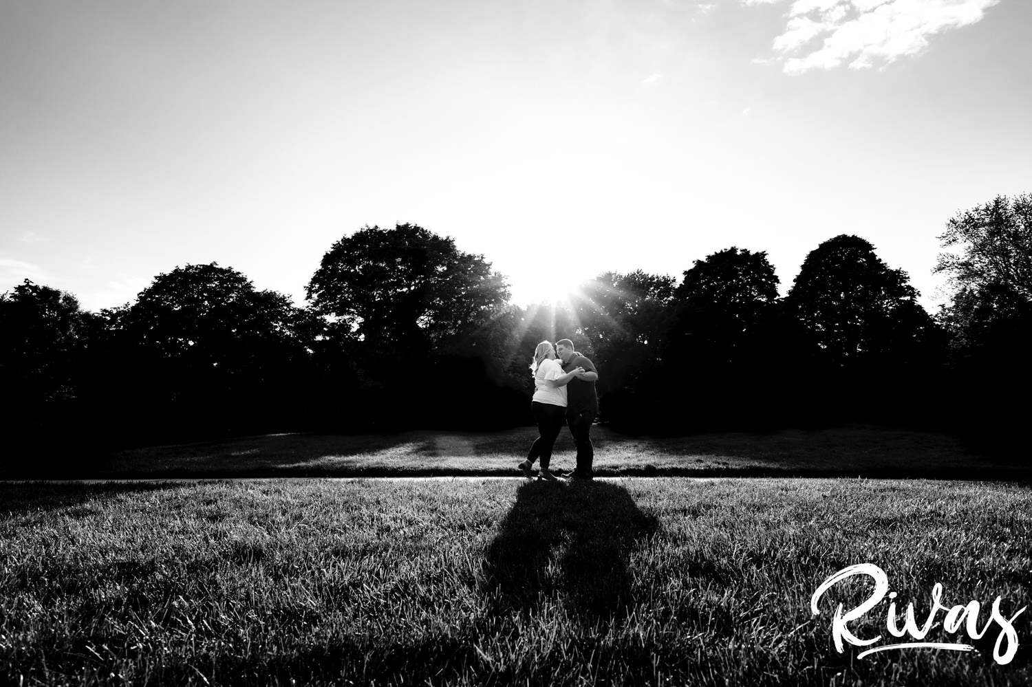A wide, black and white portrait of an engaged couple dancing in the sunlight on the sidewalk at Loose Park during their summer engagement photography session in Kansas City. 