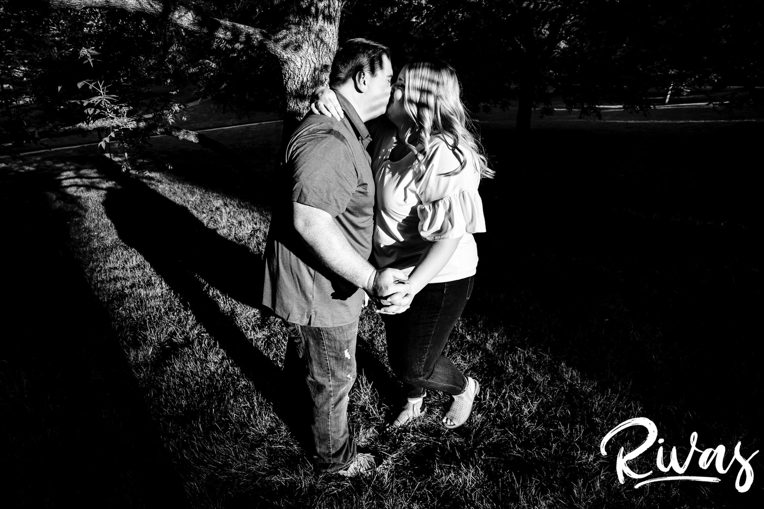 A full-length black and white picture of an engaged couple dancing together underneath a canopy of trees during their engagement photography session at Loose Park in Kansas City. 