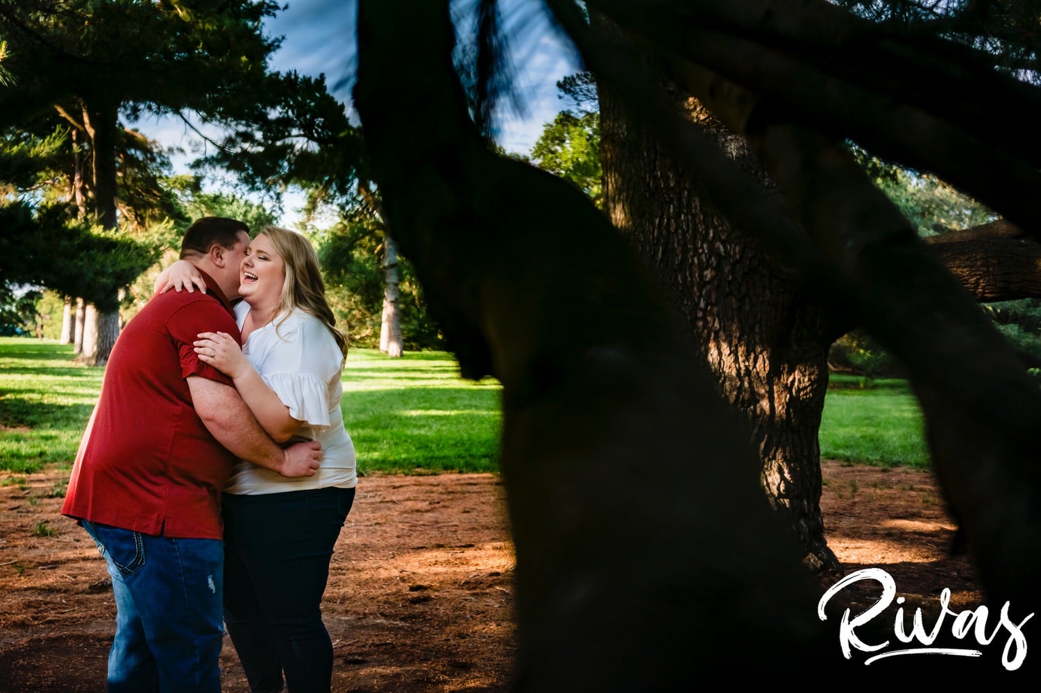 A close-up, colorful candid picture of an engaged couple laughing hysterically together surrounded by trees at Kansas City's Loose Park during their engagement photography session. 