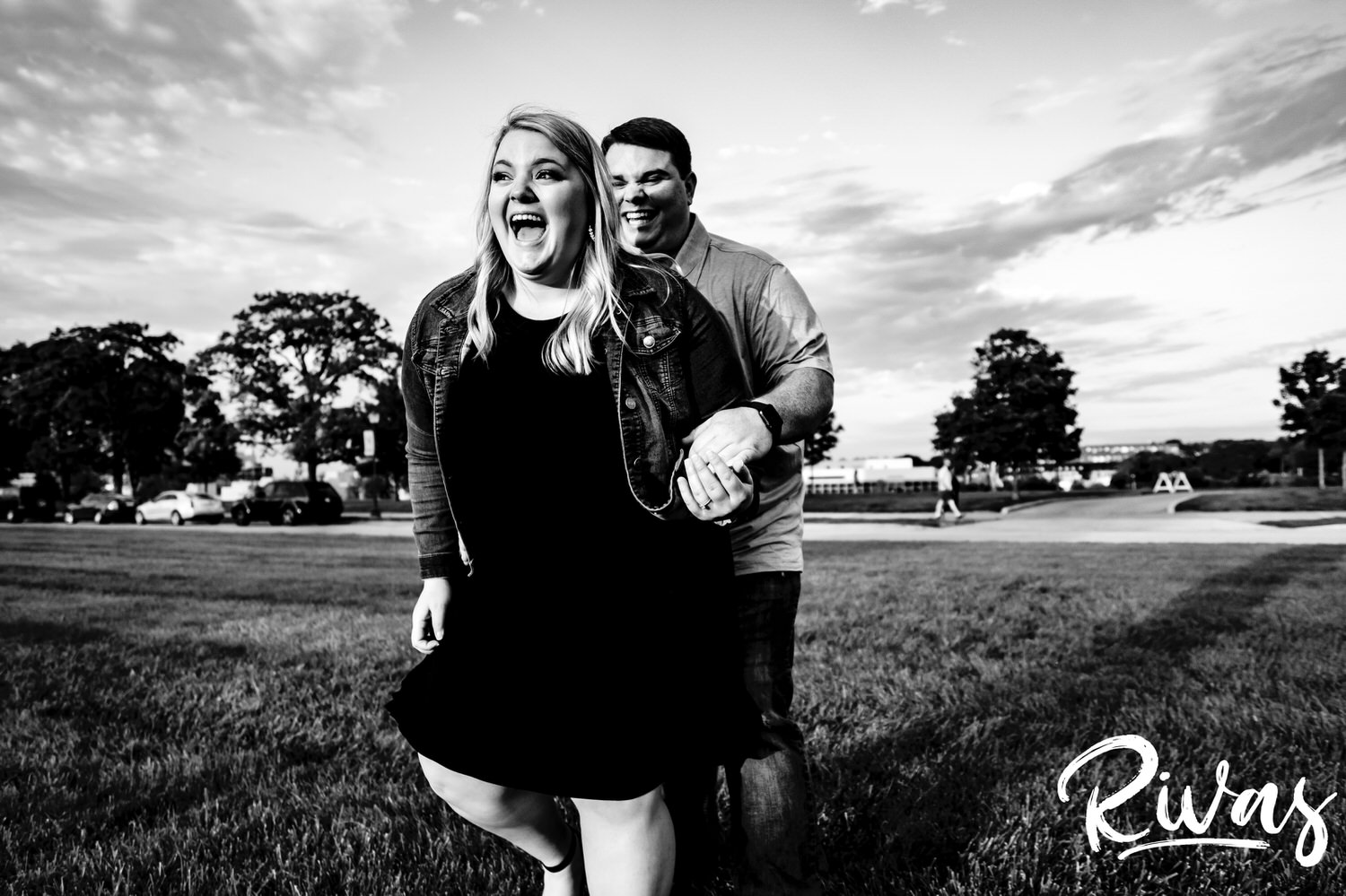 A candid black and white picture of a man tickling his fiance as she laughs hysterically and tries to scoot away during their Liberty Memorial summer engagement photography session in Kansas City. 