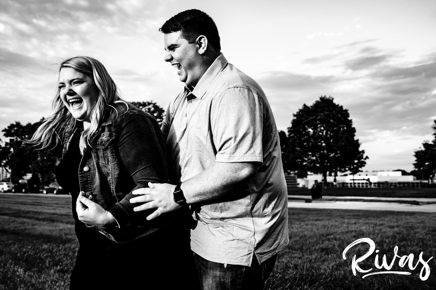 A candid black and white picture of a man tickling his fiance as she laughs hysterically and tries to scoot away during their Liberty Memorial summer engagement photography session in Kansas City.