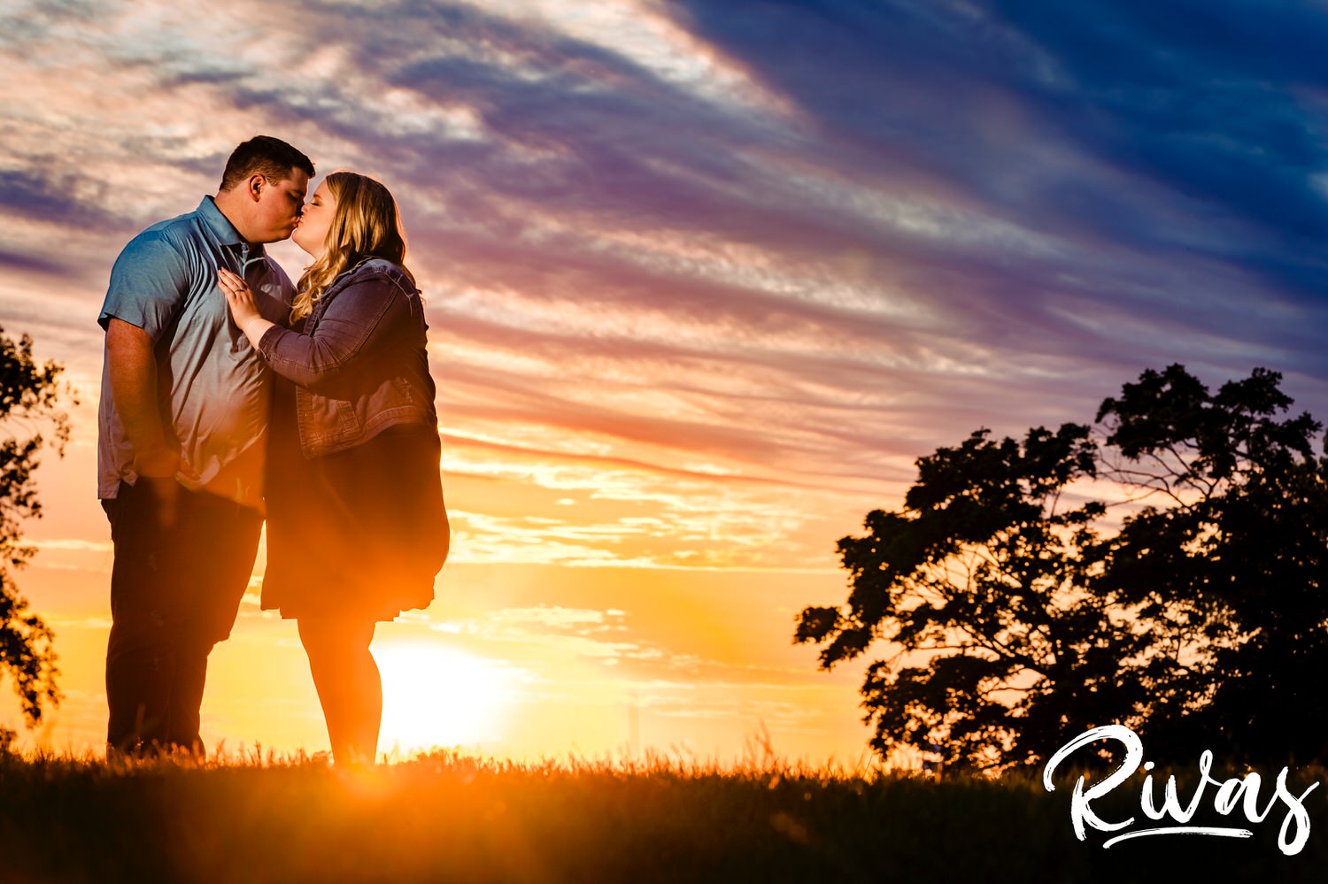 A vibrant portrait of an engaged couple sharing an embrace as the golden sun sets behind them during their summer engagement session at Kansas City's Liberty Memorial. 