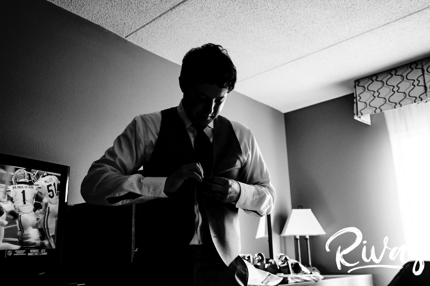 A candid black and white picture of a groom buttoning the vest of his tuxedo up on the afternoon of his fall wedding in Virginia. 