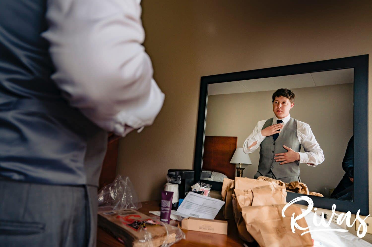 A candid picture of a groom smoothing his tie as he looks at his reflection in a large mirror on the afternoon of his fall wedding at The Barns at Hamilton Station Vineyard. 