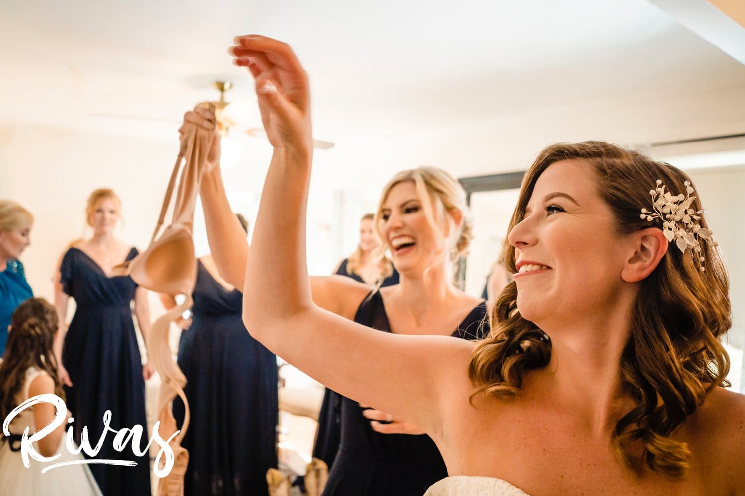 A colorful, candid picture of a bride throwing her bra over her shoulder at her sister as she holds her wedding gown up on the afternoon of her wedding at Hamilton Station Vineyard. 