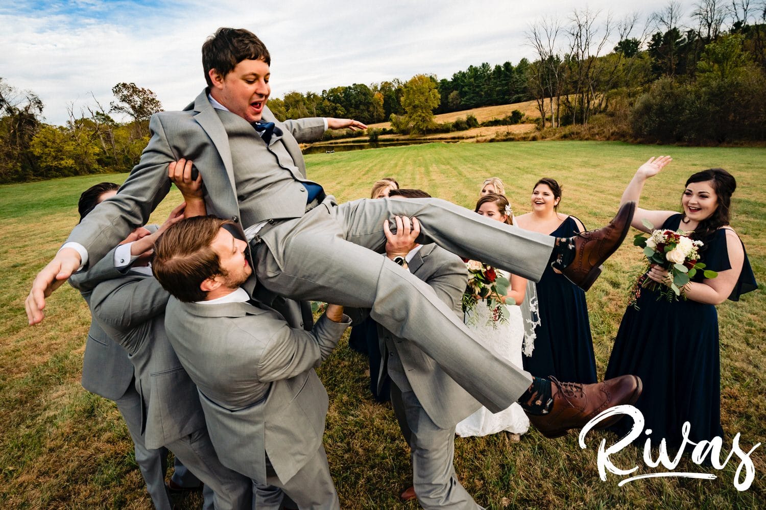 A colorful, candid picture of a groom's groomsmen lifting him into their air in the middle of a field on his fall wedding day at The Barns at Hamilton Station Vineyard. 