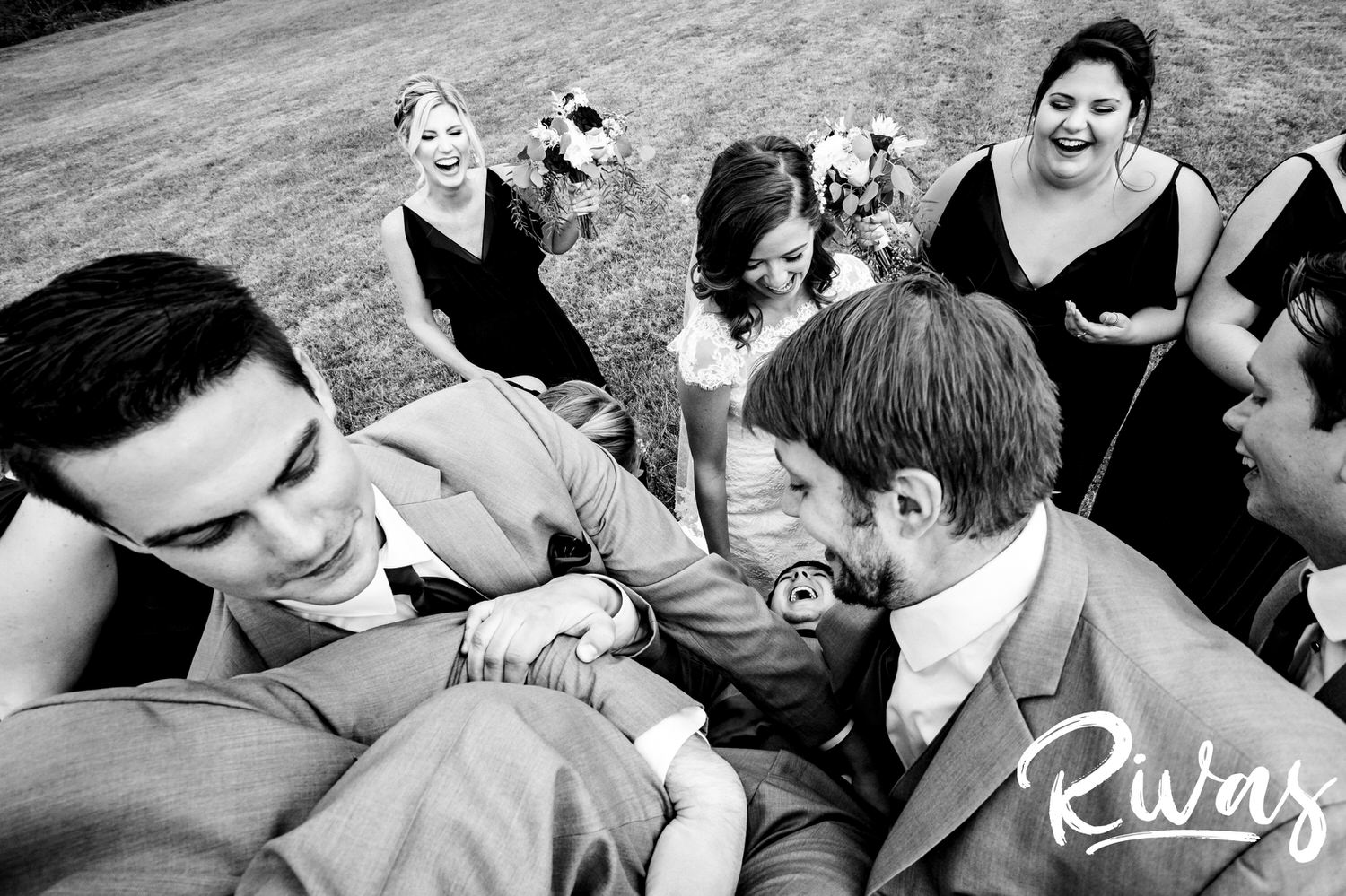 A candid black and white picture taken from above an upside down groom of his bride and her bridesmaids looking at him laughing on the afternoon of their fall wedding day at The Barns at Hamilton Station Vineyard. 