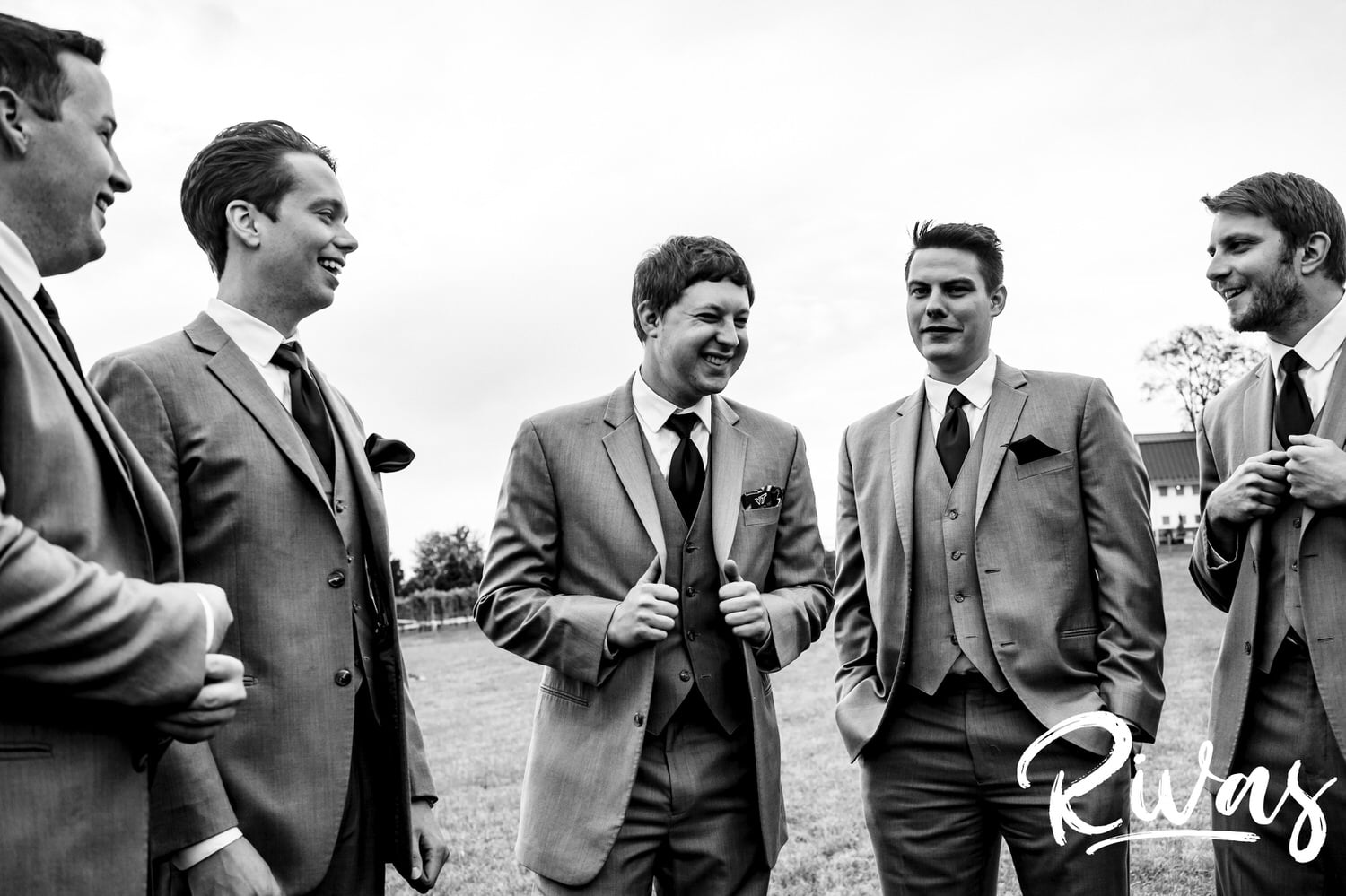 A black and white, candid picture of a groom and his groomsmen standing together laughing on the afternoon of his fall wedding at The Barns at Hamilton Station Vineyard. 
