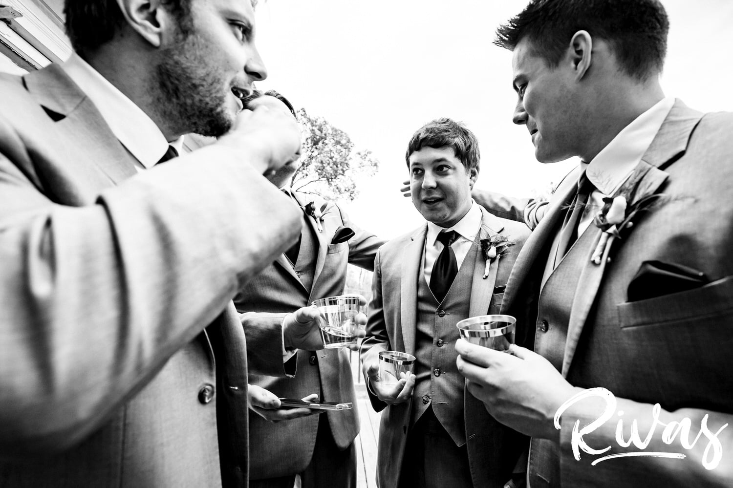 A candid black and white picture of a groomsmen clustered with his groomsmen, telling stories on the afternoon of his fall wedding. 