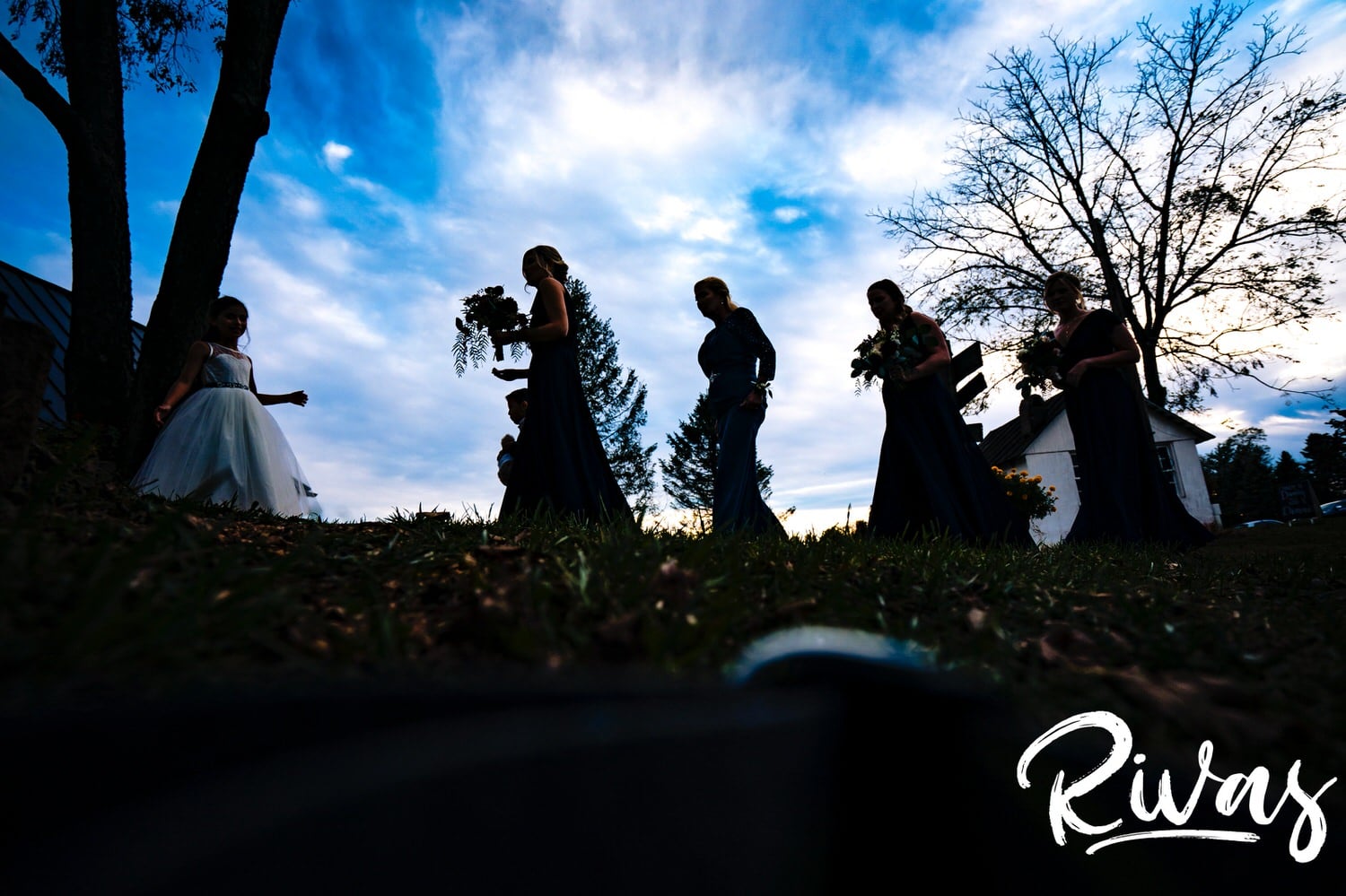 A colorful, silhouetted picture of a bride and her bridesmaids walking across the lawn at The Barns at Hamilton Station Vineyard on her fall wedding day. 
