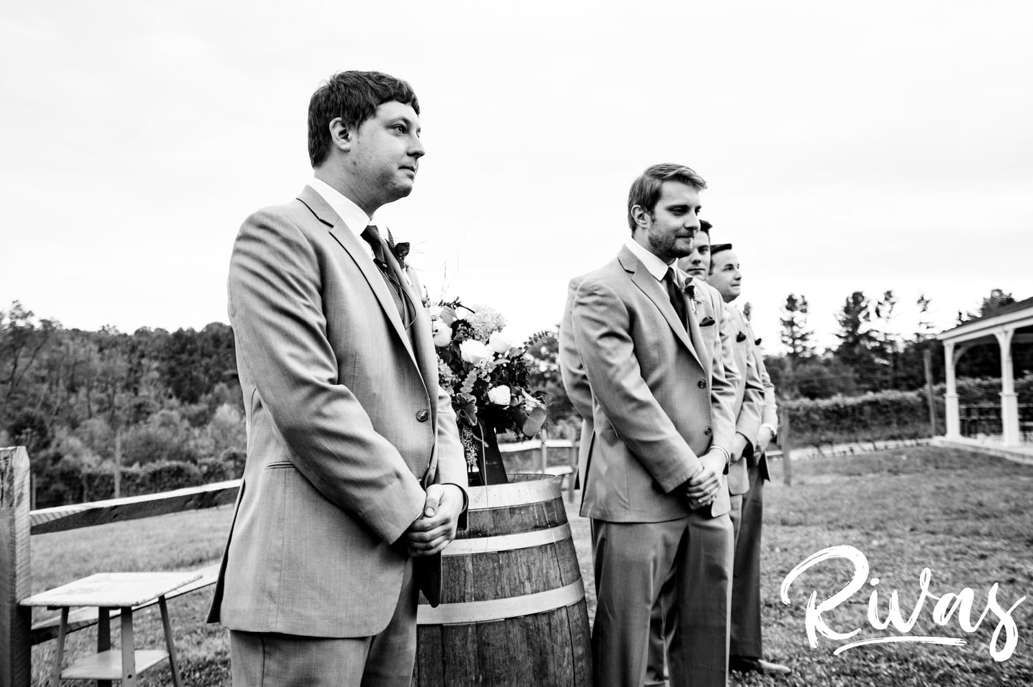 A candid black and white picture of a groom and his groomsmen waiting at the front of the aisle during his wedding ceremony. 