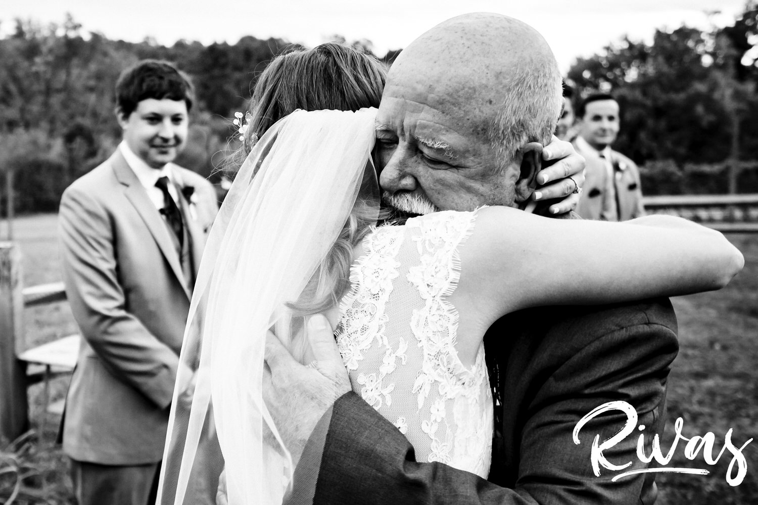 An emotional black and white picture of a bride hugging her dad as he gives her away at the end of the aisle during her fall wedding ceremony. 