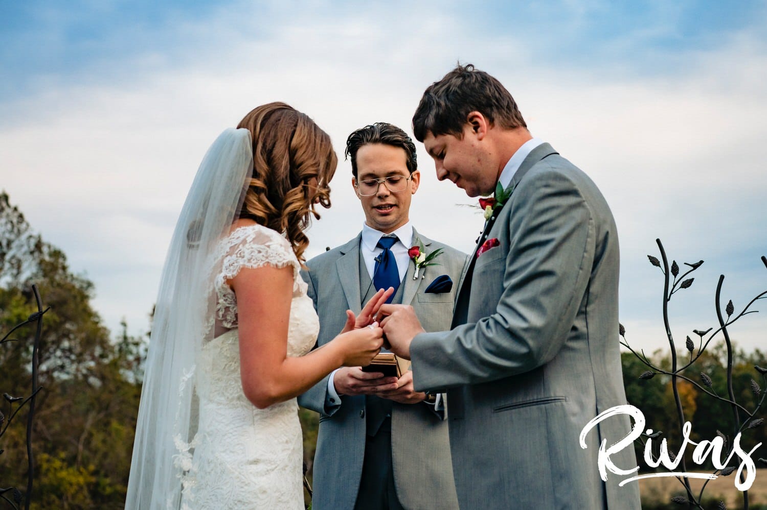 A colorful picture of a groom putting a wedding band on his bride's finger during their fall wedding ceremony. 