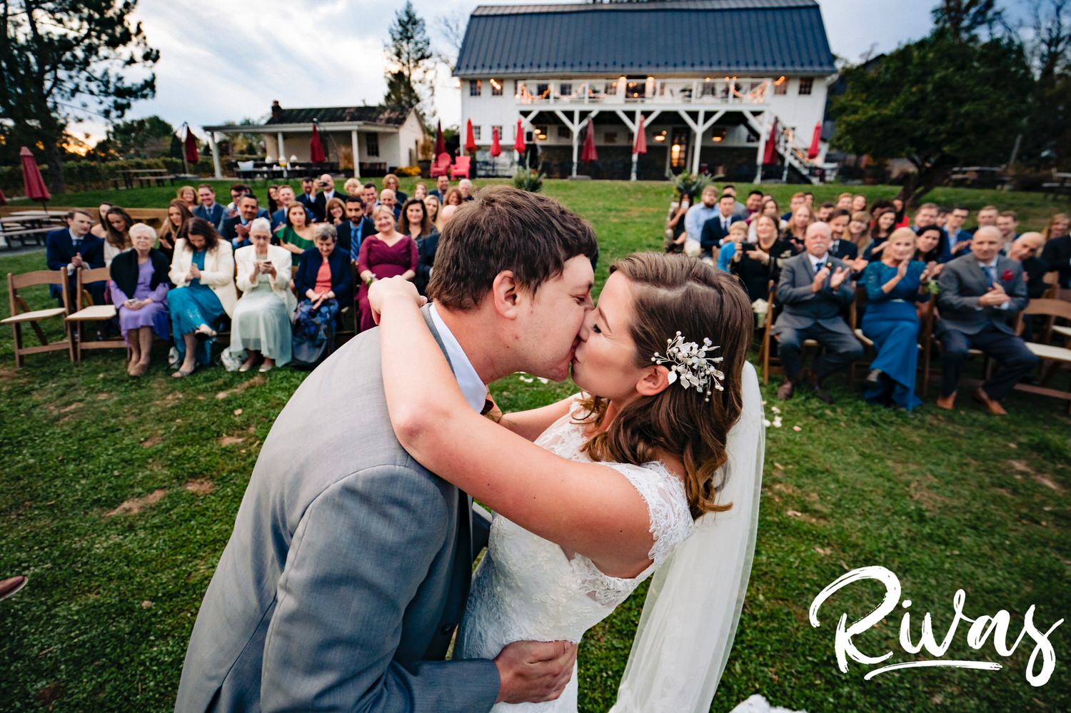 A colorful picture of a bride and groom sharing their first kiss taken from behind the altar, looking back at their wedding guests during a fall wedding at The Barns at Hamilton Station Vineyard. 