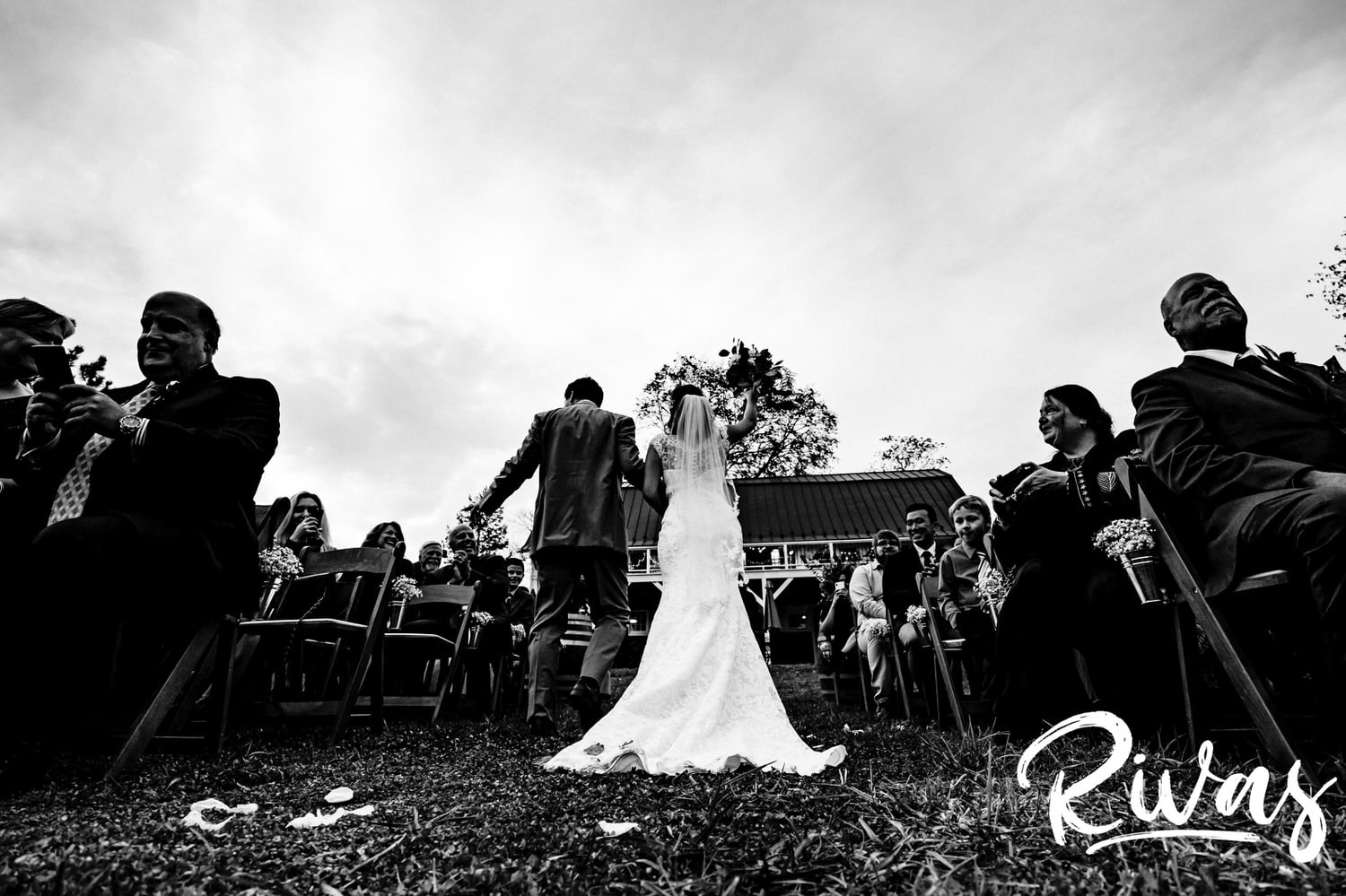 A dramatic black and white picture taken from the ground looking up of a bride and groom walking back up the aisle after their fall wedding ceremony at The Barns at Hamilton Station Vineyard. 